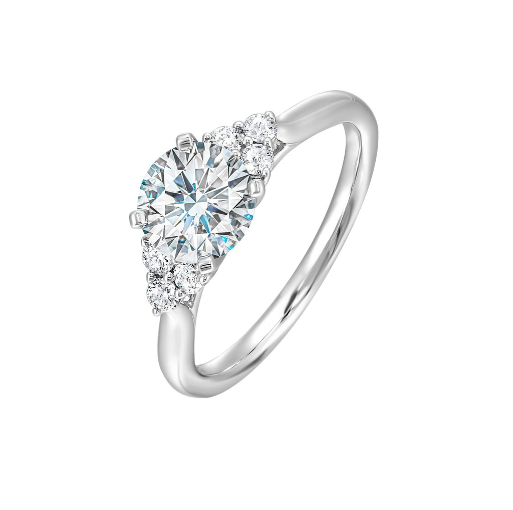 Three stone ring features a trinity of diamonds on either side, focusing the round solitaire at center, is a symbol of everlasting love.